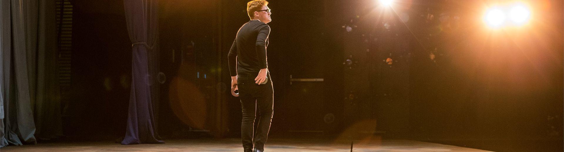 An actor standing on stage under spotlights.