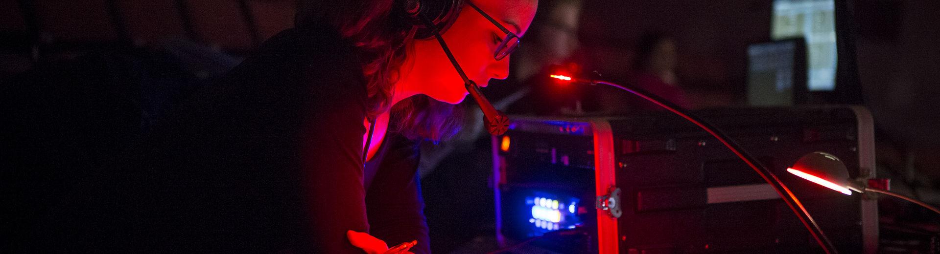 A woman with a headset reads in a darkened room backstage.