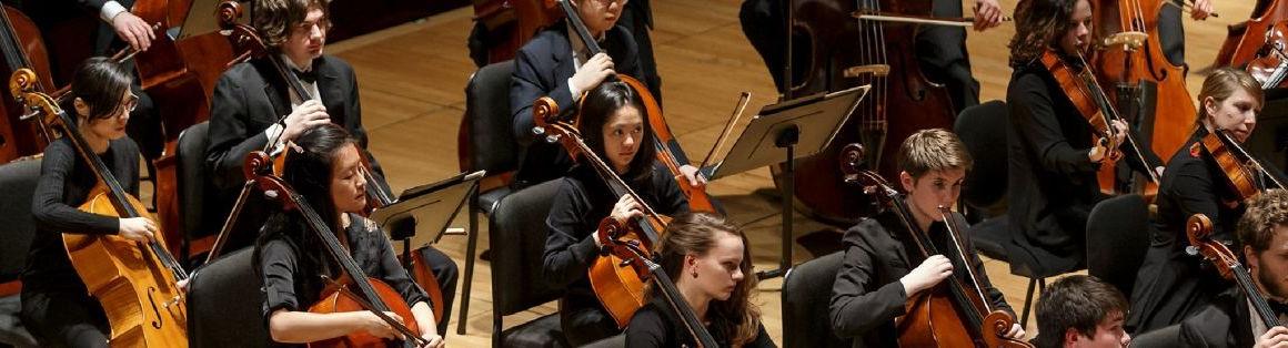 A student string orchestra is shown mid-performance. All musicians are dressed in formalwear.