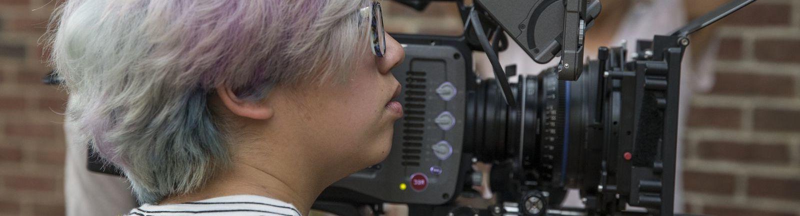 A student filming with two students looking on from the other side.