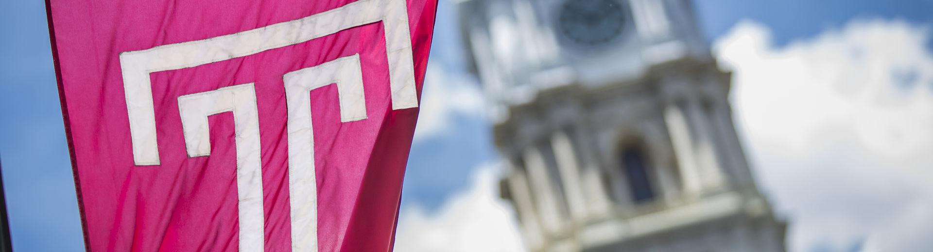 The cherry red Temple T flag waving in front of Philadelphia City Hall on a sunny day.