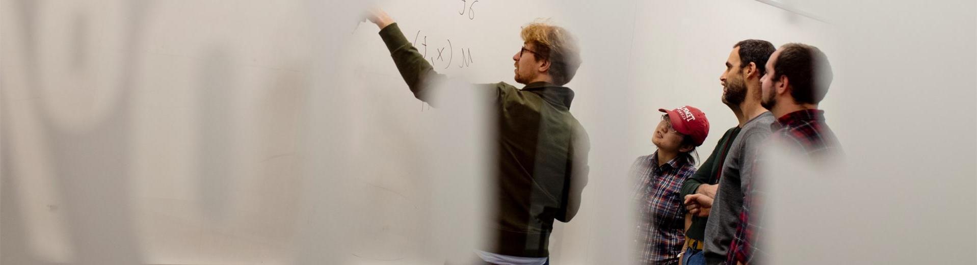 Students pointing to a math equation on a white board in a College of Science and Technology classroom.