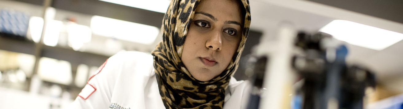 A student wears a white coat while working in a lab.