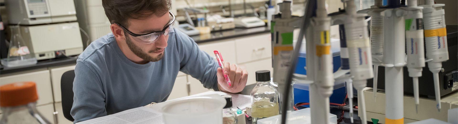 Temple student sitting over book, highlighter in hand, in a College of Science and Technology laboratory.