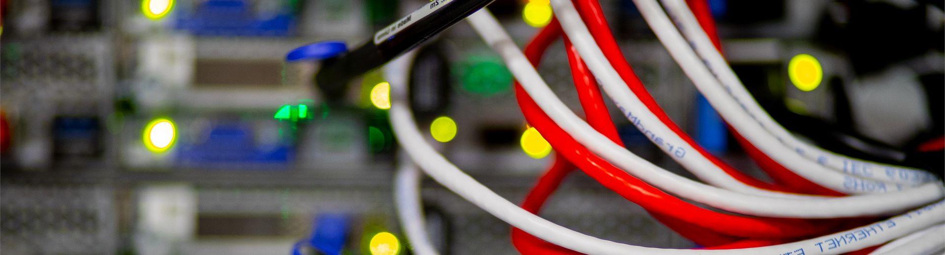 Red and white strands of computer cable fanning out from the back of a stack of servers.