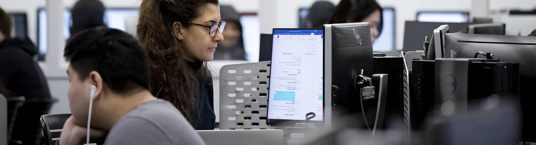 A woman sitting and looking at a computer screen in a technology lab.