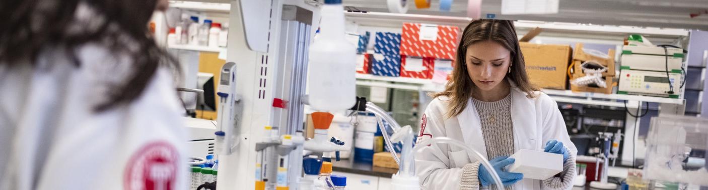 Two Katz students wearing white lab coats doing research in a lab