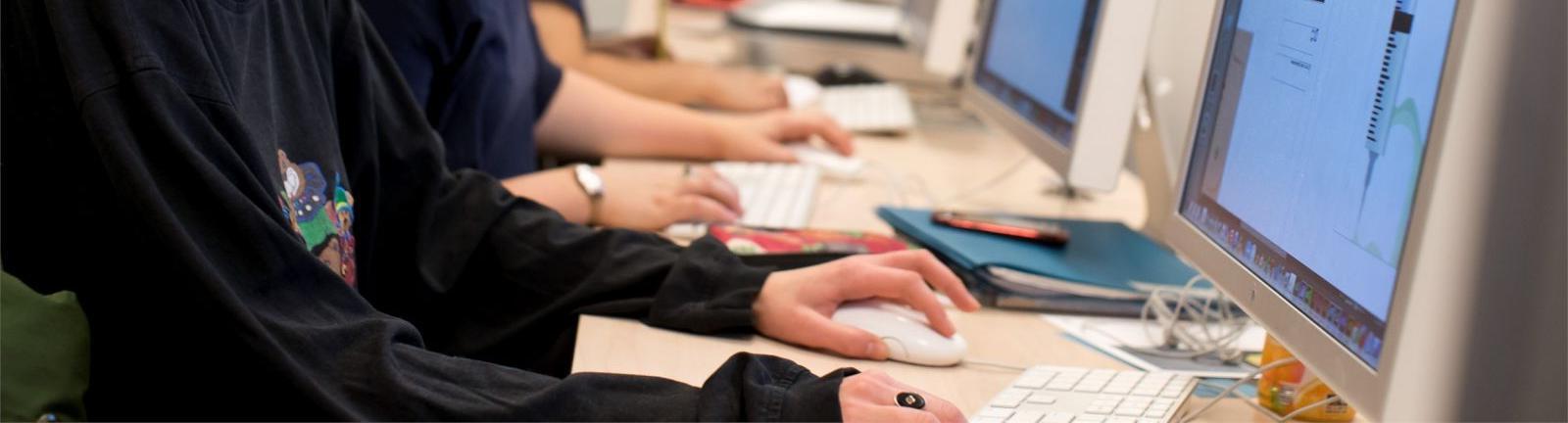 Girl with glasses sitting in front of a computer screen with hands on keyboard in a lab at Temple.