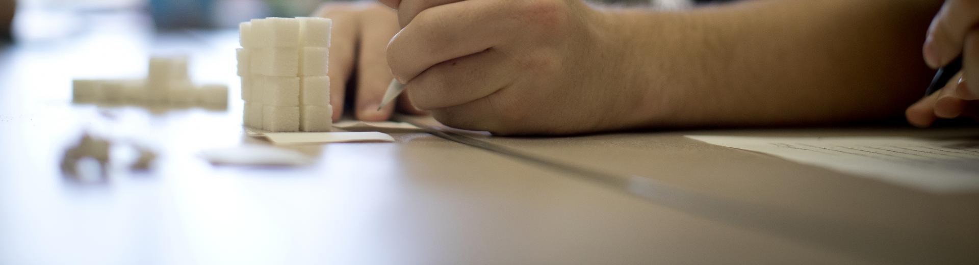 Student writing in a classroom with stack of sugar cubes