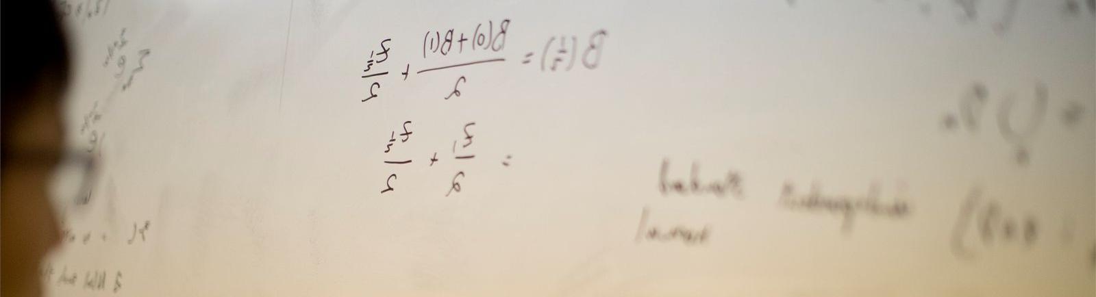 Student writing math equation on white board in a College of Science and Technology classroom.