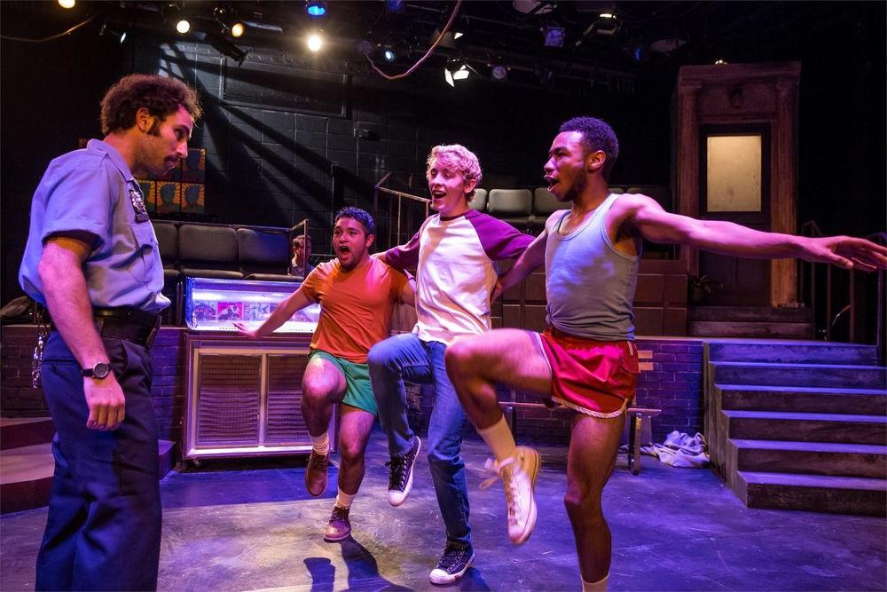 Three guys dance 和 sing on stage with another actor looking on.