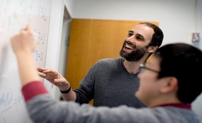 一位皇冠体育的教授在教室里帮助学生在白板上解数学方程.