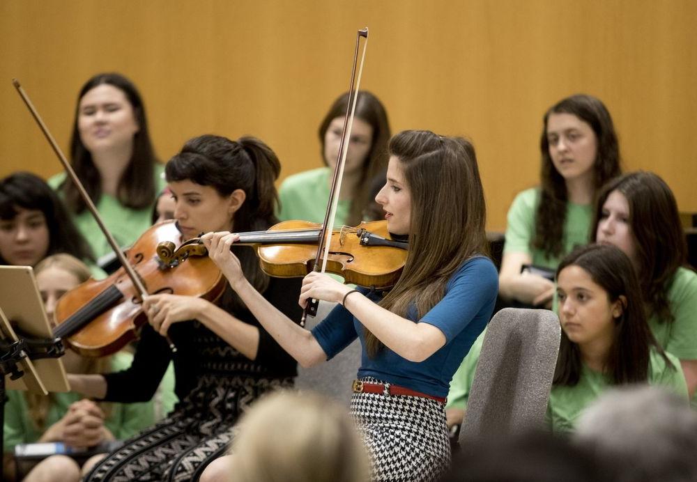 Two women play violin for students.