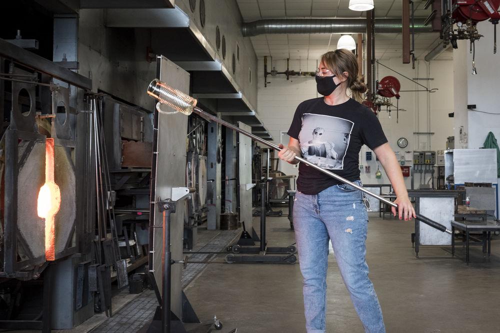 student inserting glass blowing instrument into the kiln. 