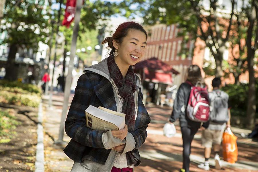 Student holding books standing on university campus path